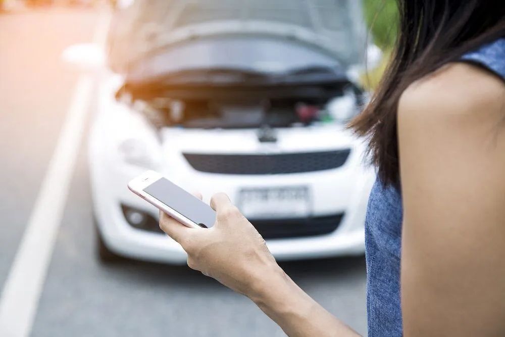 A Woman Is Holding a Cell Phone in Front of A Broken Down Car c