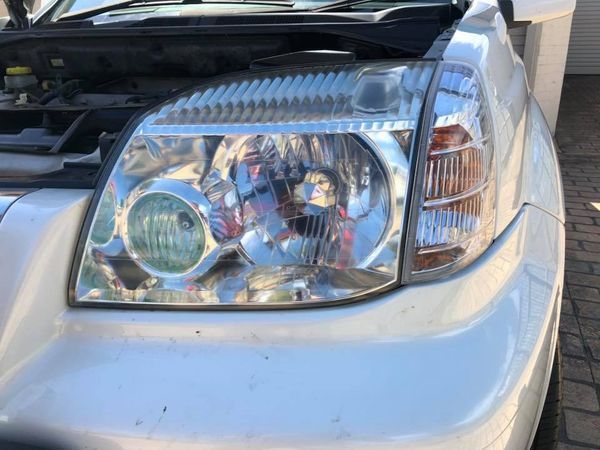 Close-up of a silver car’s front headlight and bumper with the hood open