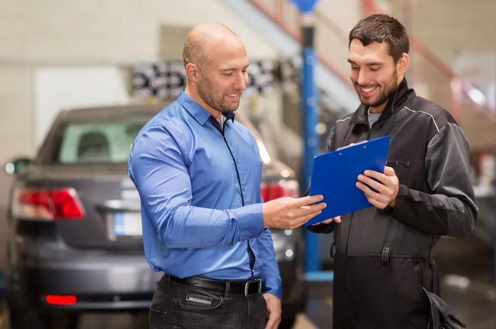 Two Men Are Looking At A Clipboard In A Garage — Bay City Quality Mobile Mechanic In Pialba, QLD