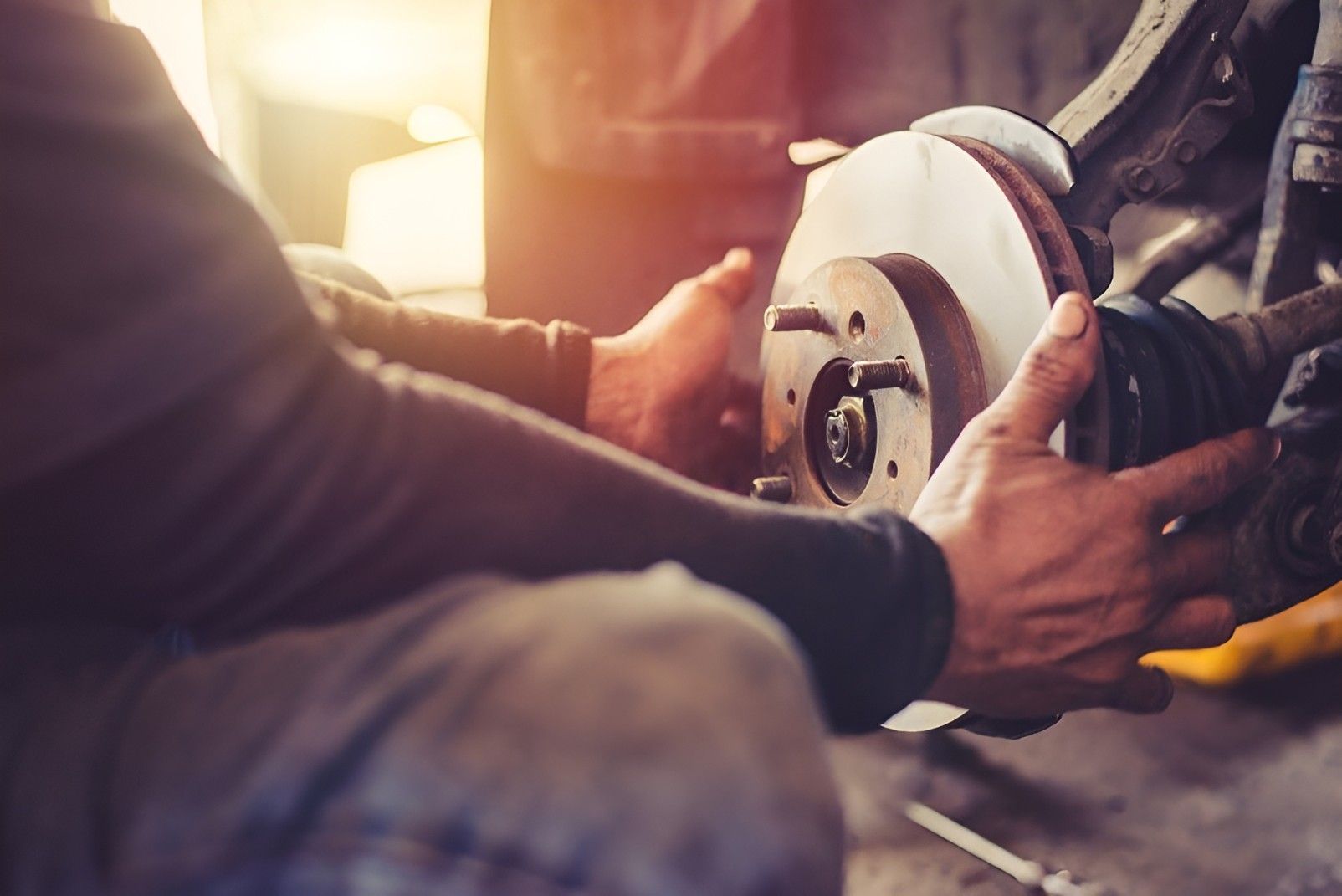 A Man Is Fixing A Brake Disc On A Car In A Garage With His Bare Hands — Bay City Quality Mobile Mechanic In Pialba, QLD