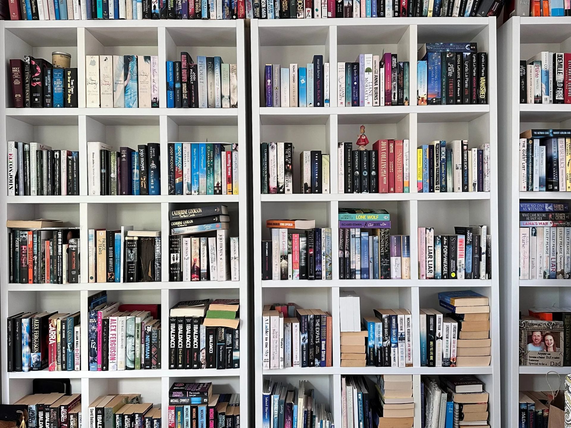 Three white, grid-style bookcases filled with many books of various colors, sizes, and orientations.