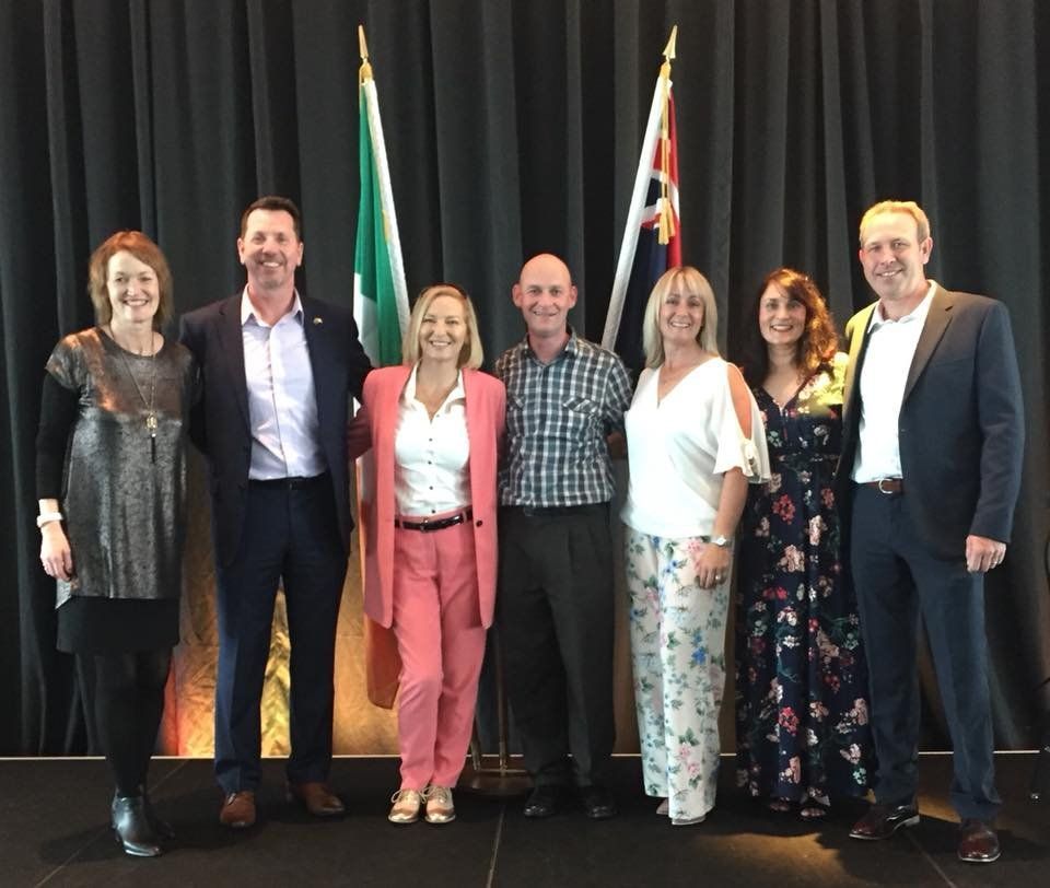 Seven people pose for a group photo in front of two flags and a black curtain.