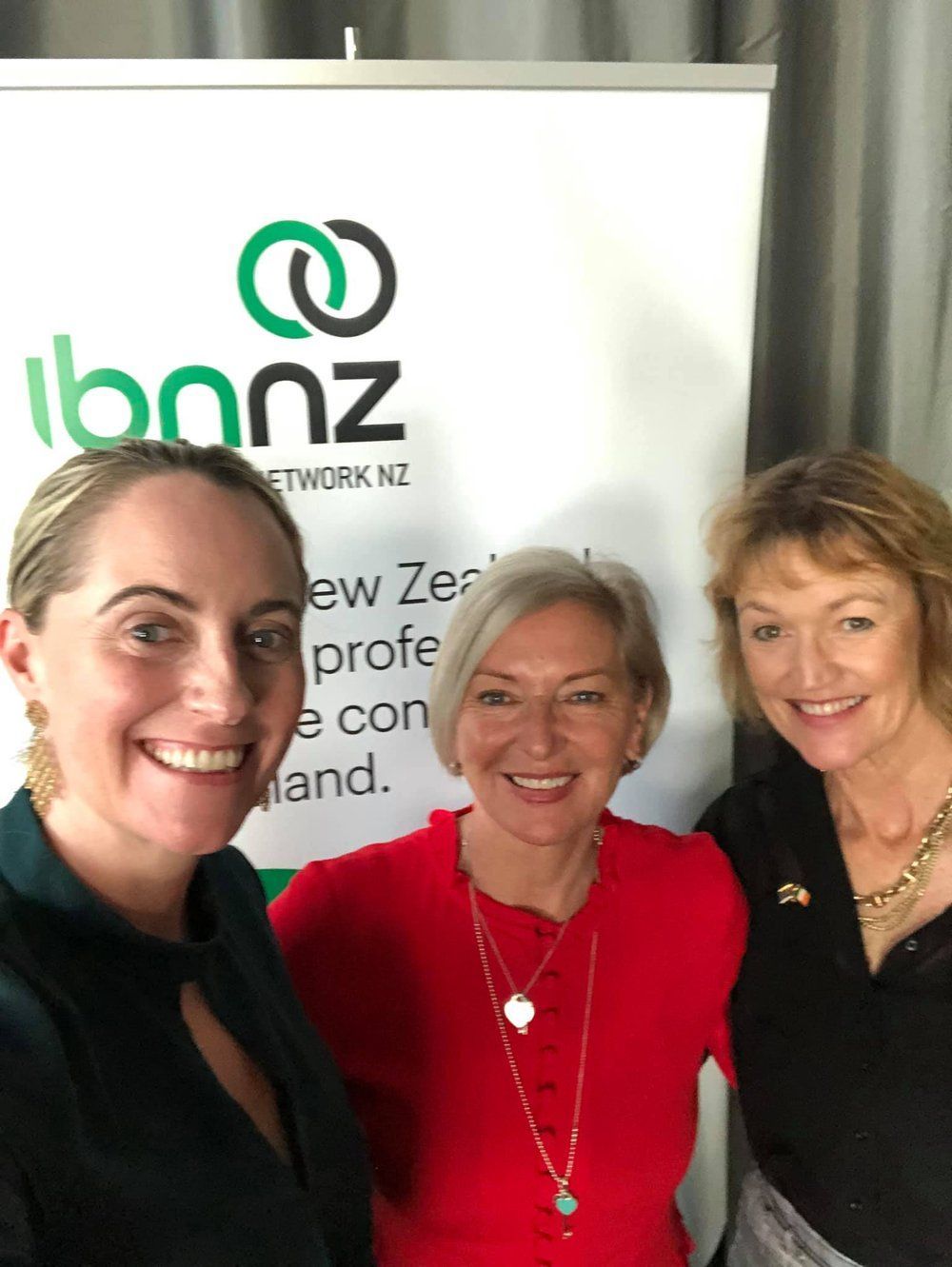 Three smiling people pose for a photo in front of an 