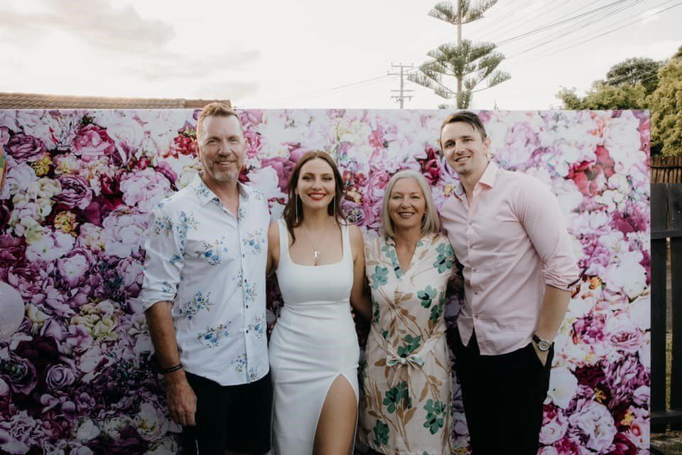 Four people stand together posing for a photo in front of a vibrant floral backdrop.