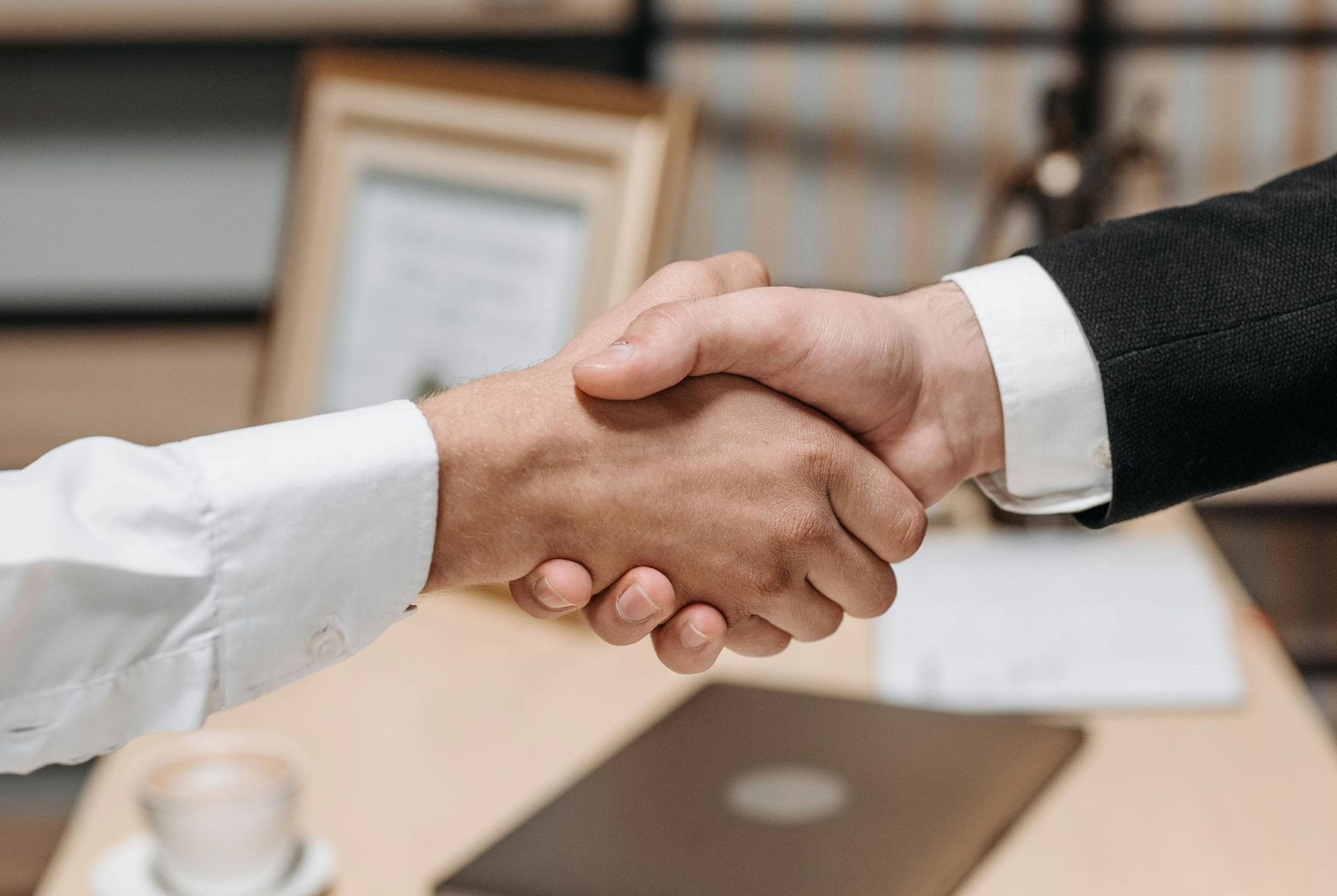 Two people shaking hands over a desk in an office setting.