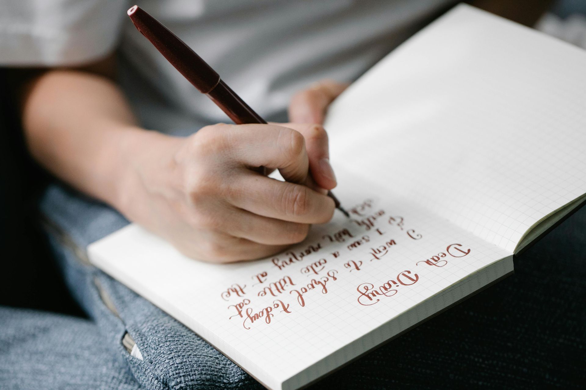 A person writes in a notebook with a dark pen, with their hand in focus over the handwritten journal entry.