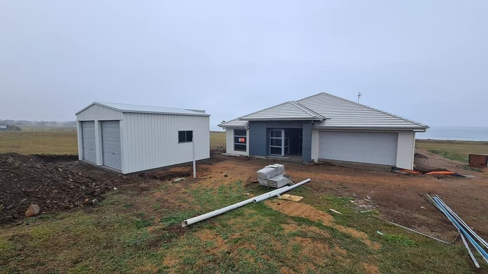 A House Is Being Built In A Field Next To A Garage — Bushman Sheds in Bundaberg East, QLD