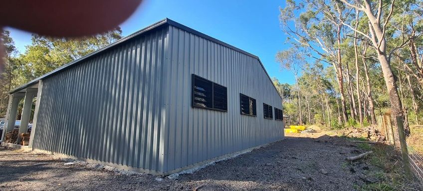 A Large Gray Metal Shed Is Built In The Middle Of A Forest — Bushman Sheds in Bundaberg East, QLD