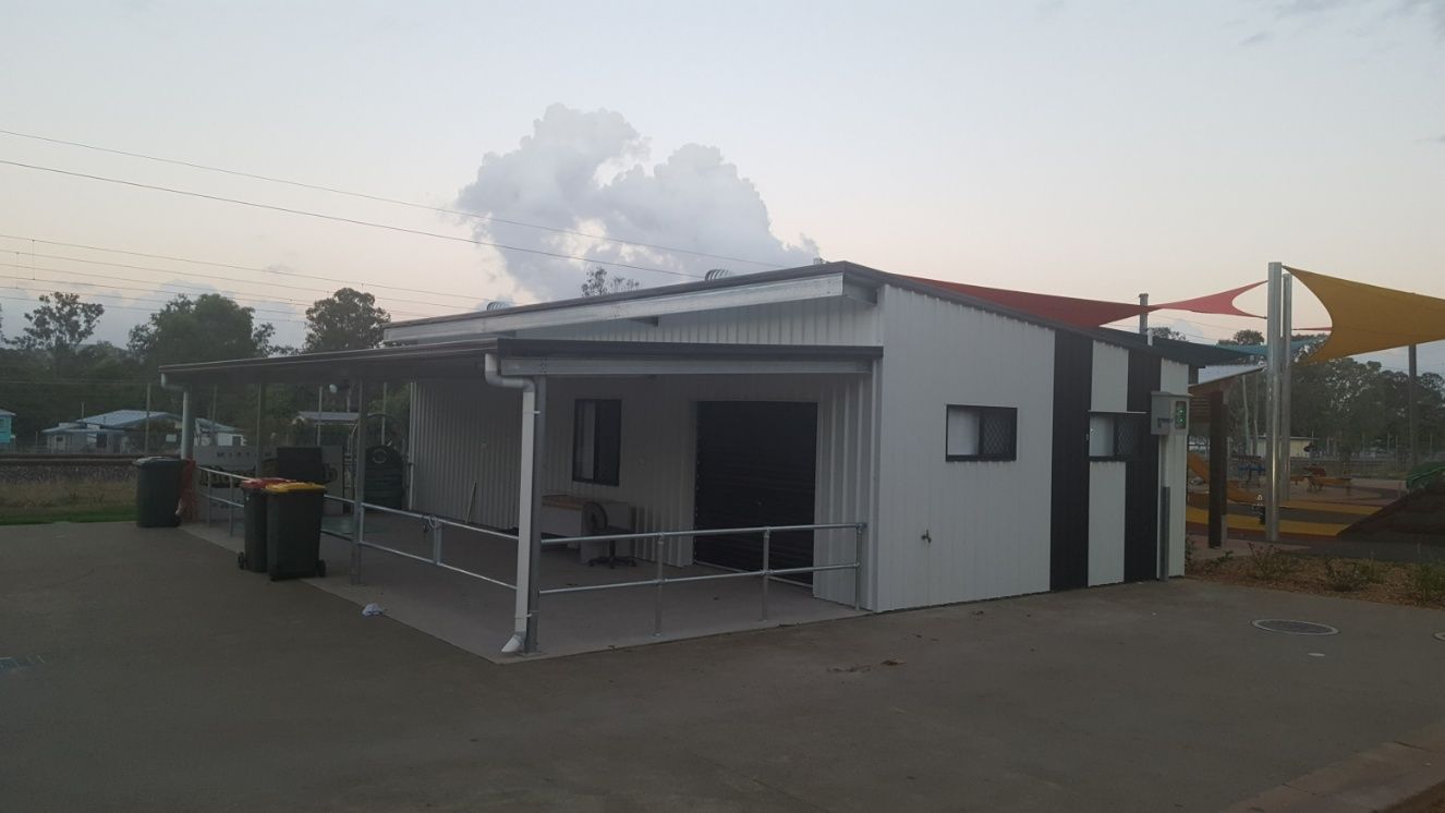 A Small White Shed With A Red Roof And A Covered Porch — Bushman Sheds in Bundaberg East, QLD