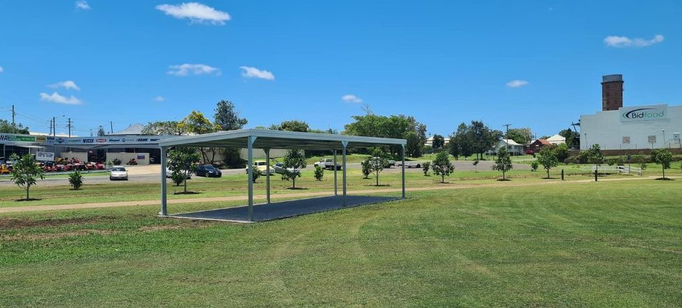 A Large Grassy Field With A Covered Area In The Middle Of It — Bushman Sheds in Bundaberg East, QLD