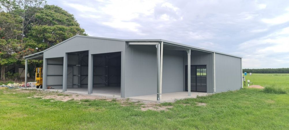 A Large Gray Building Is Sitting In The Middle Of A Grassy Field — Bushman Sheds in Bundaberg East, QLD