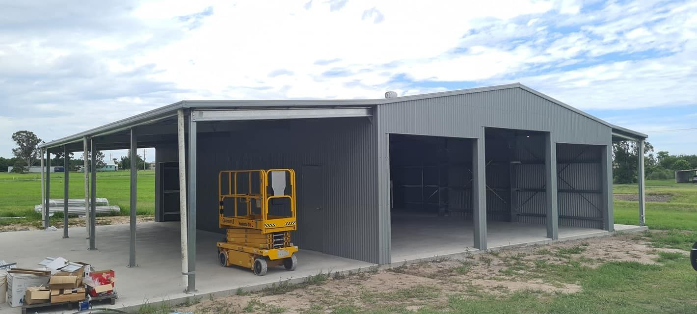 A Yellow Scissor Lift Is Parked In Front Of A Large Metal Building — Bushman Sheds in Bundaberg East, QLD
