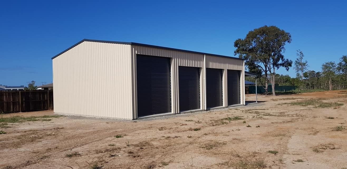 A Metal Shed With Three Garage Doors Is Built In The Middle Of A Dirt Field — Bushman Sheds in Bundaberg East, QLD