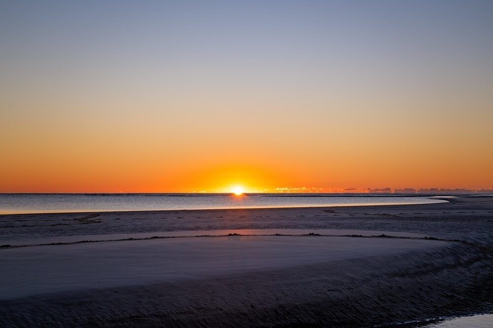 The Sun Is Setting Over The Ocean On A Beach — Bushman Sheds in Woodgate, QLD