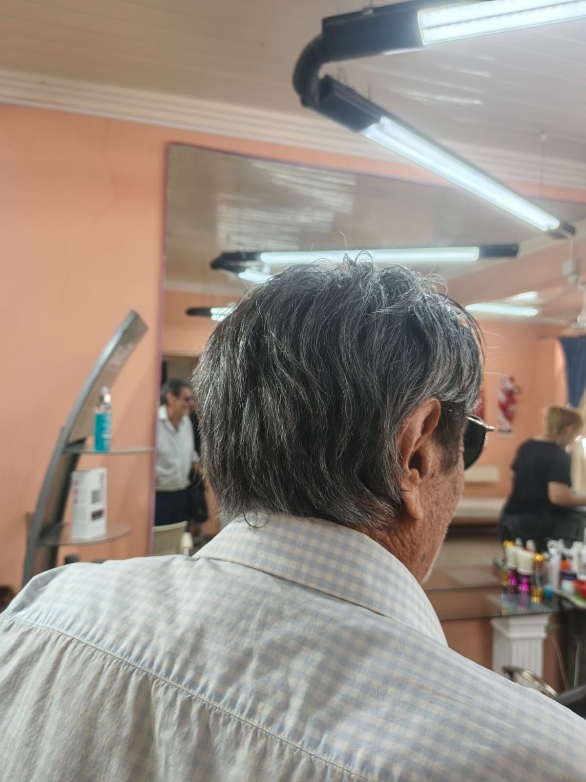 Una persona que viste una camisa de cuadros abotonada de color claro está sentada dentro de una peluquería muy iluminada.