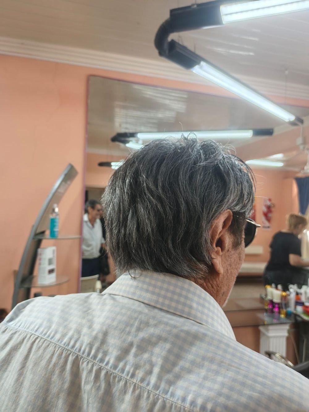 Una persona que viste una camisa de cuadros abotonada de color claro está sentada dentro de una peluquería muy iluminada.