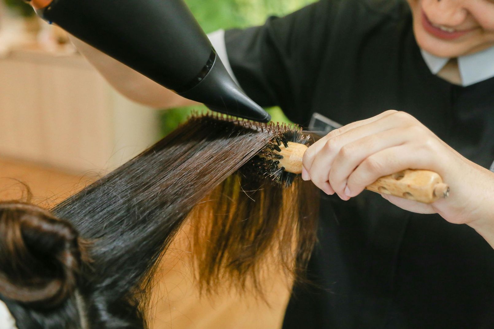 Un estilista utiliza un cepillo redondo y un secador de pelo para peinar el cabello largo y oscuro.