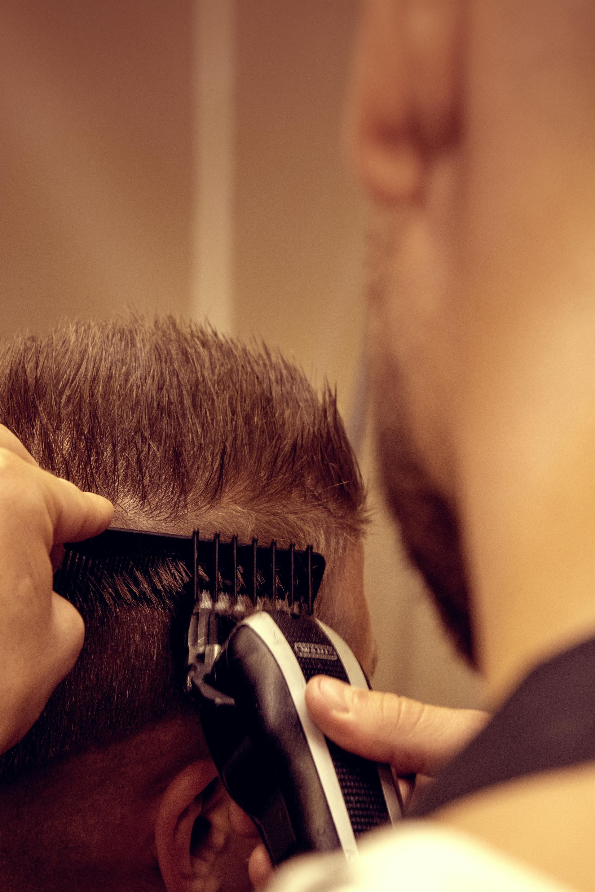 Un barbero utiliza una maquinilla eléctrica para recortar el pelo cerca de un peine que sostiene contra la cabeza del cliente.