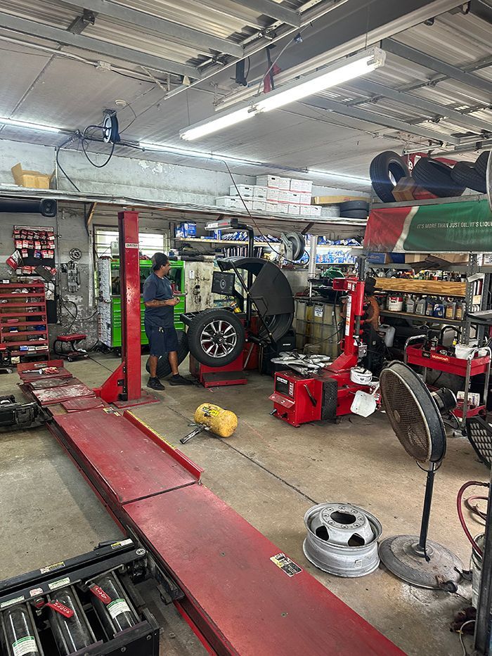 A technician works in an auto repair shop with a vehicle lift, tire changing equipment, and various mechanical tools. | Military Brake & Alignment Services Inc.