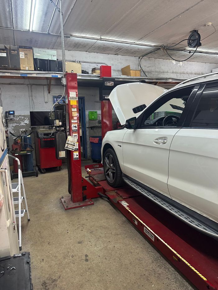 A white car with its hood raised, parked on a red hydraulic lift inside an auto repair shop. | Military Brake & Alignment Services Inc.