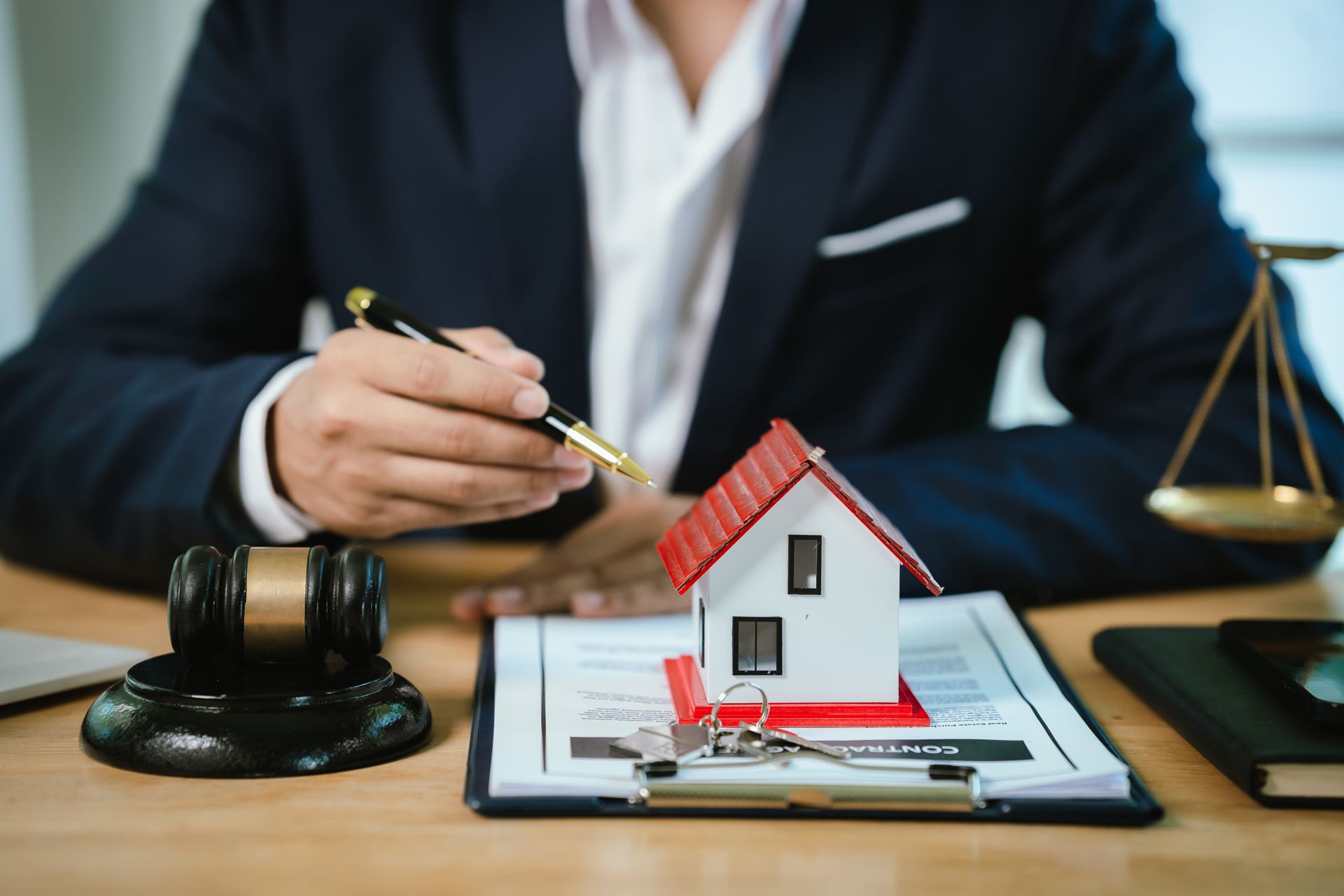 Real estate agent pointing at house model and paperwork beside a gavel and scales of justice