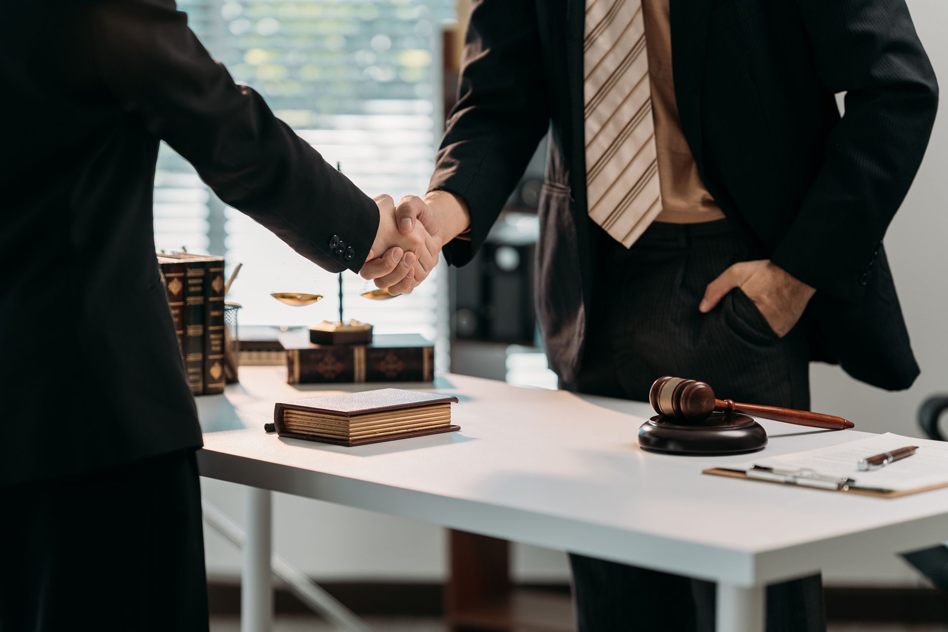Two businesspeople shaking hands across an office desk with a gavel and documents
