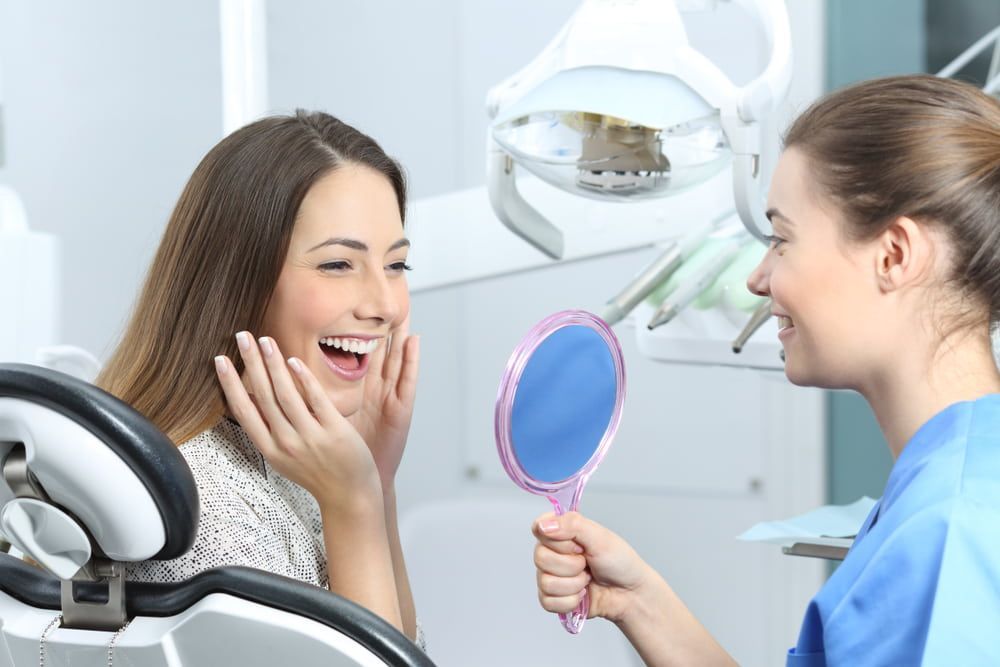 Woman Admires Her Smile in A Mirror Held by A Dentist — Dentistry Services in Cairns, QLD
