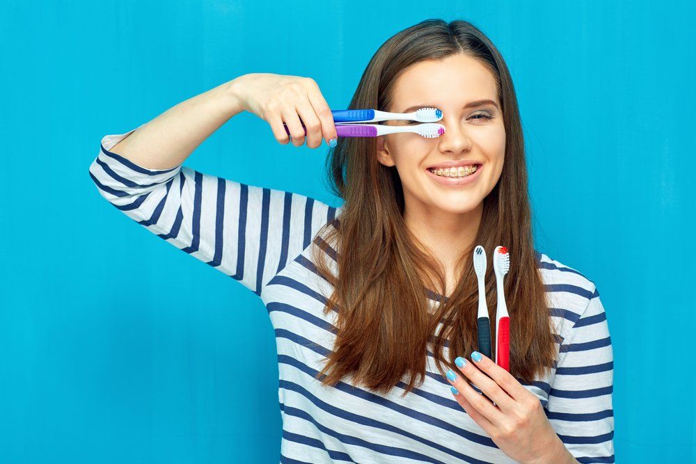 Girl With Braces Holding Tooth Brushes — Dentistry Services in Cairns, QLD