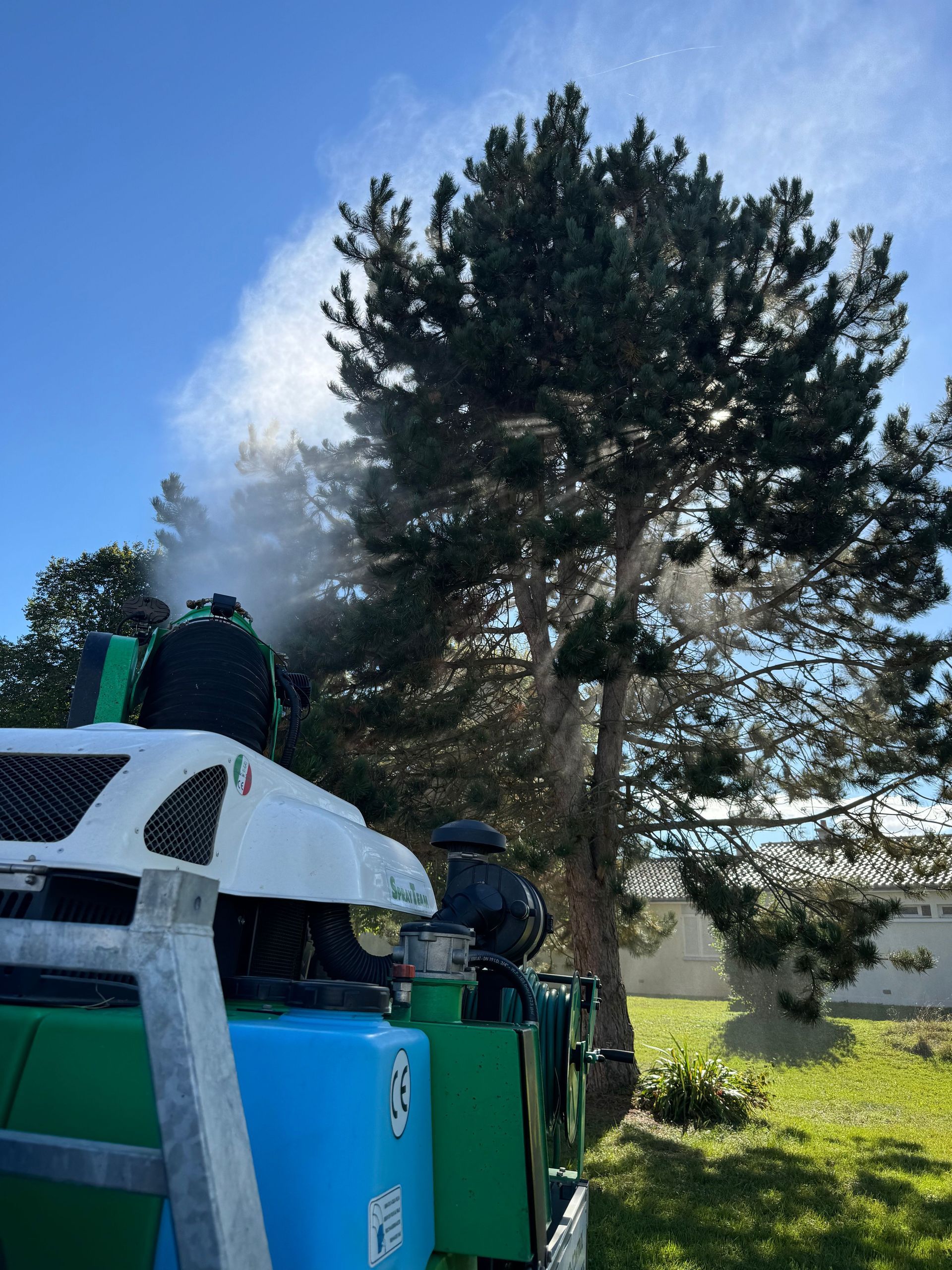 Une machine pulvérise de l'eau sur un arbre dans une cour.