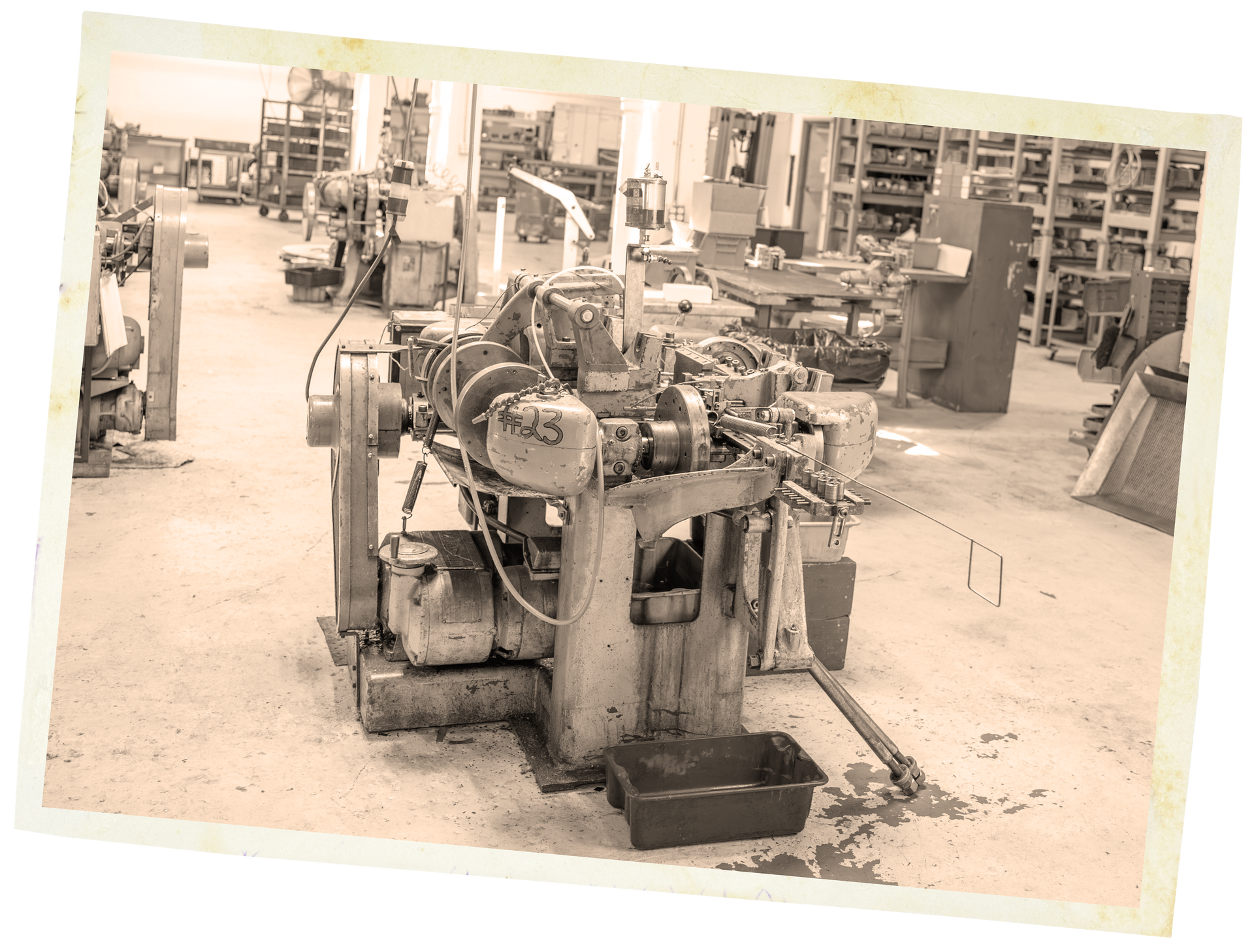 A large, industrial machine in a workshop, surrounded by other equipment. Sepia-toned.