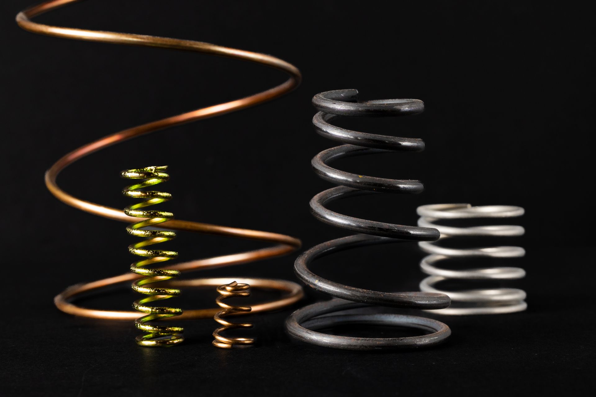 Various metal springs in different sizes, shapes, and colors, displayed against a black background.
