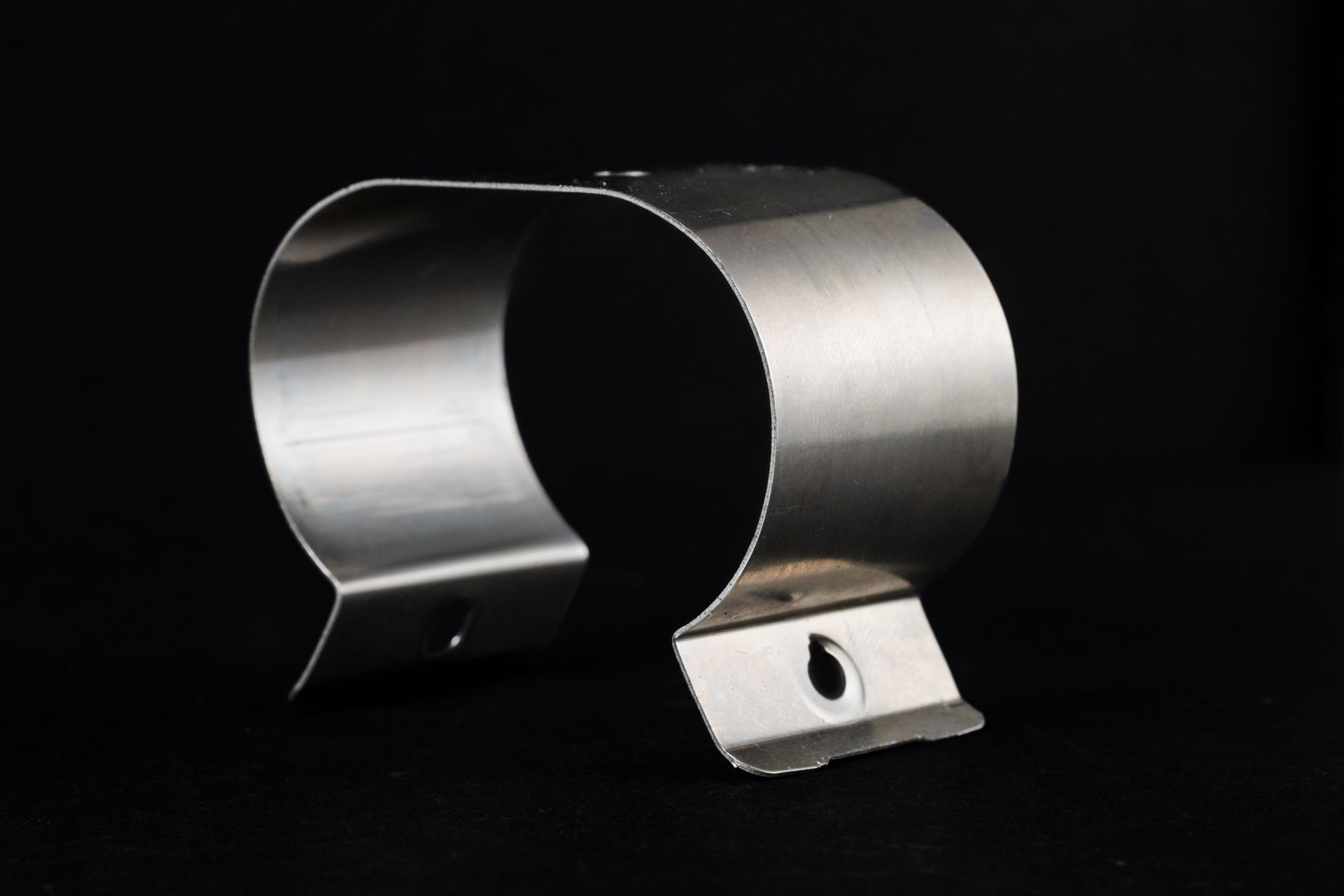 Curved metal clamp with two tabs and holes, against a black background.