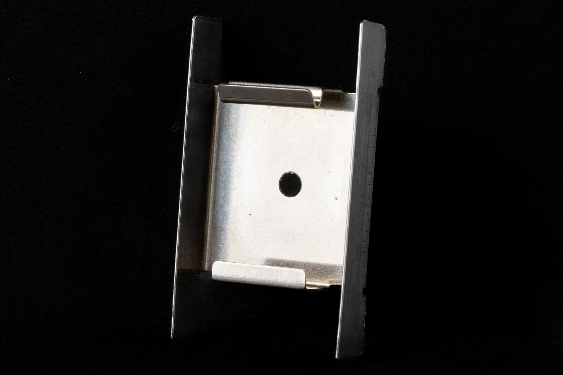 Silver metal bracket with a central hole, on a black background.