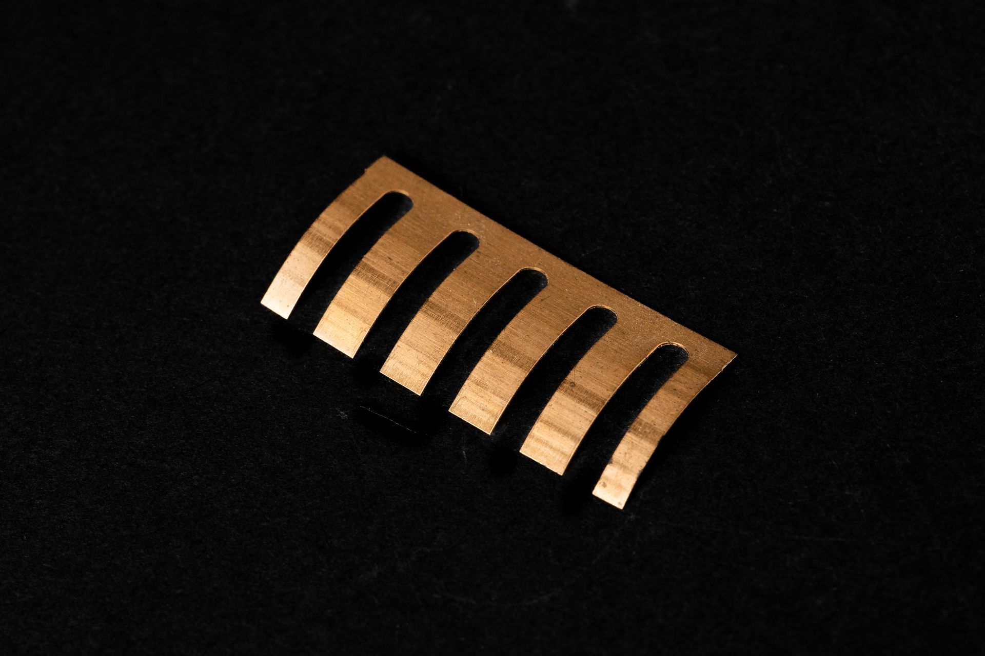 Copper-colored metal comb-like piece with curved tines, resting on a black surface.