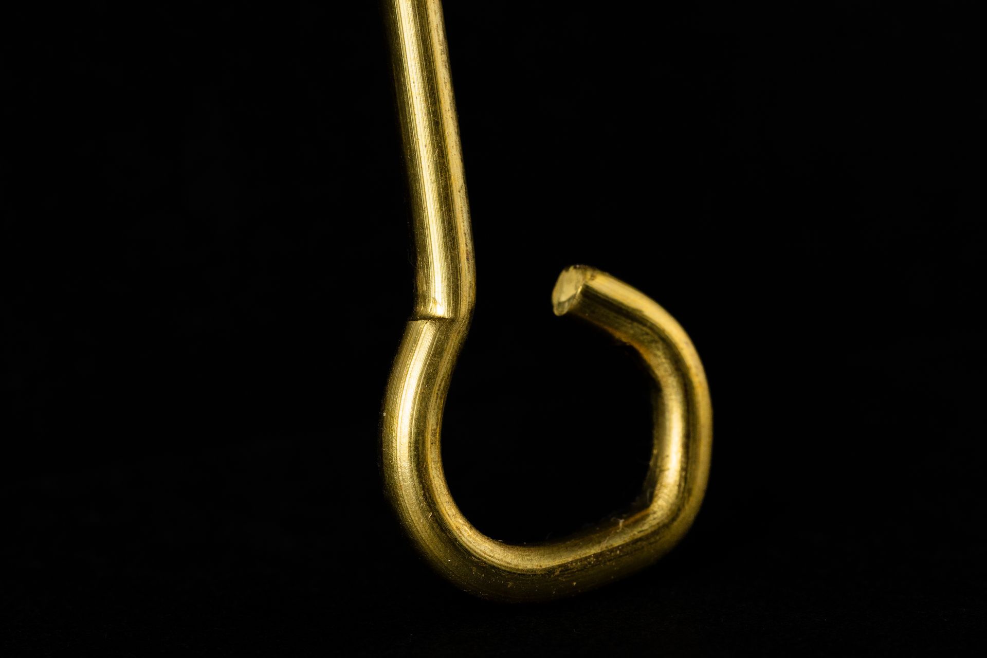 Golden, hooked metal object against a black background.