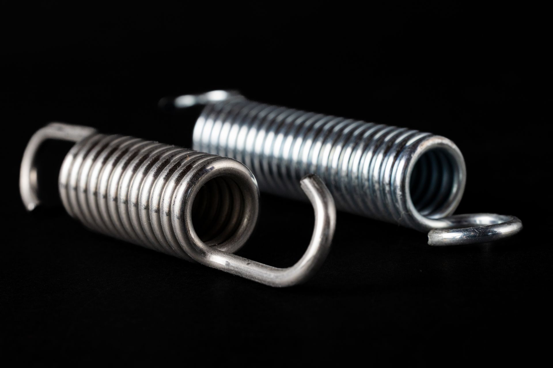Two metal springs with hooked ends, resting against a black background.