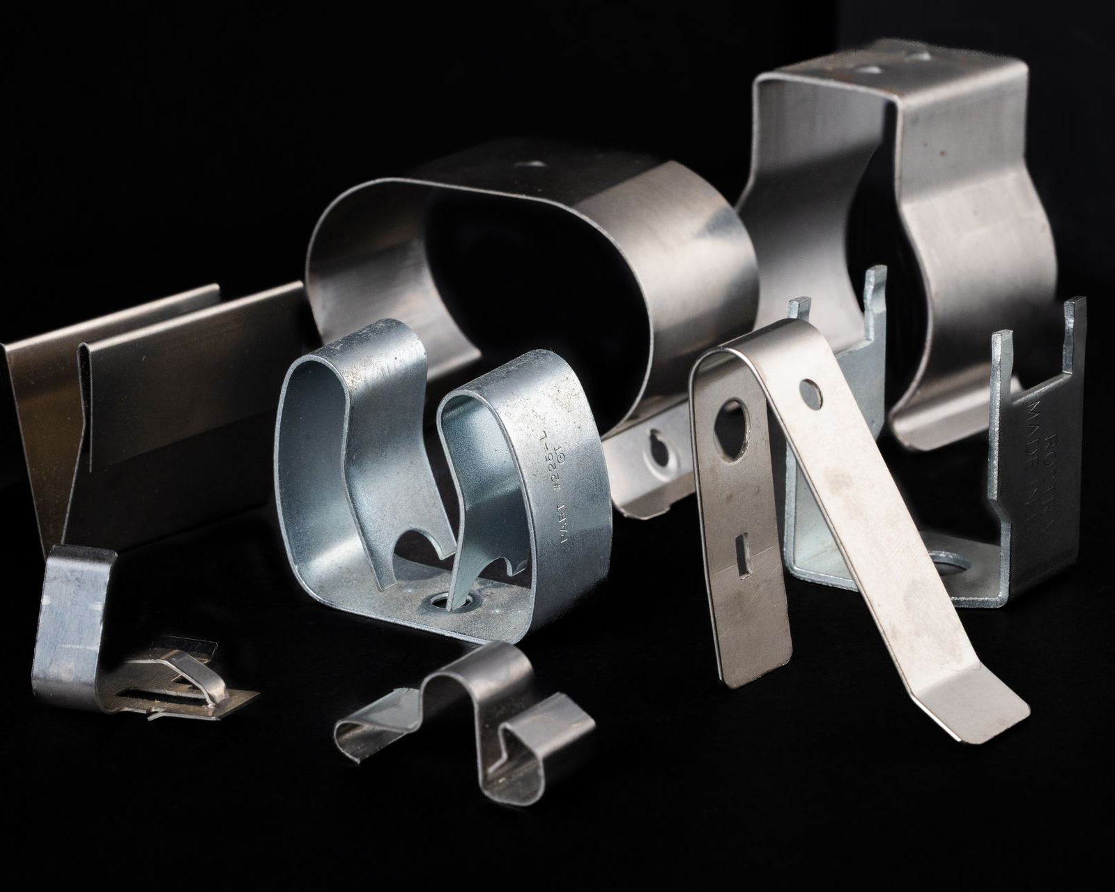 Various steel spring clips, bent into different shapes, against a black background.