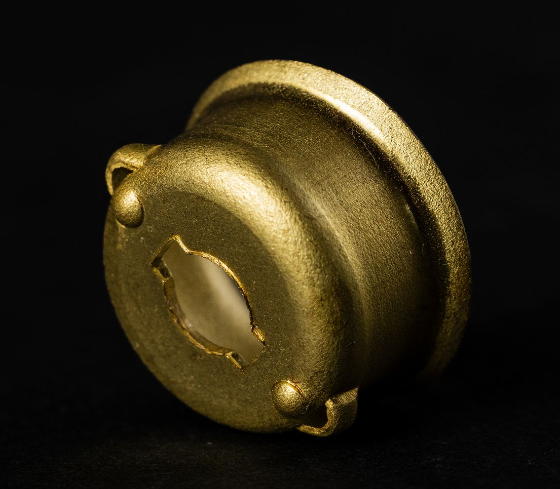 Golden metal bowl-shaped object with a rough texture and a cut-out section, set against a black background.