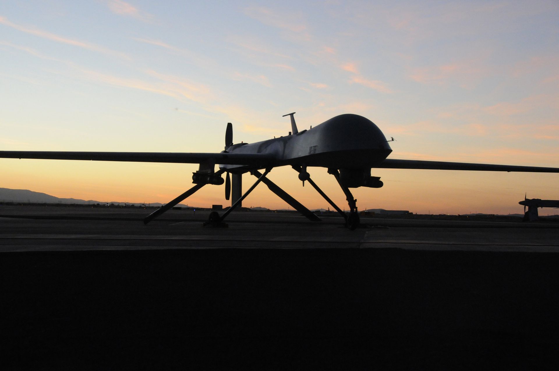 Silhouette of a drone on a runway at sunset; wings spread; landing gear visible.