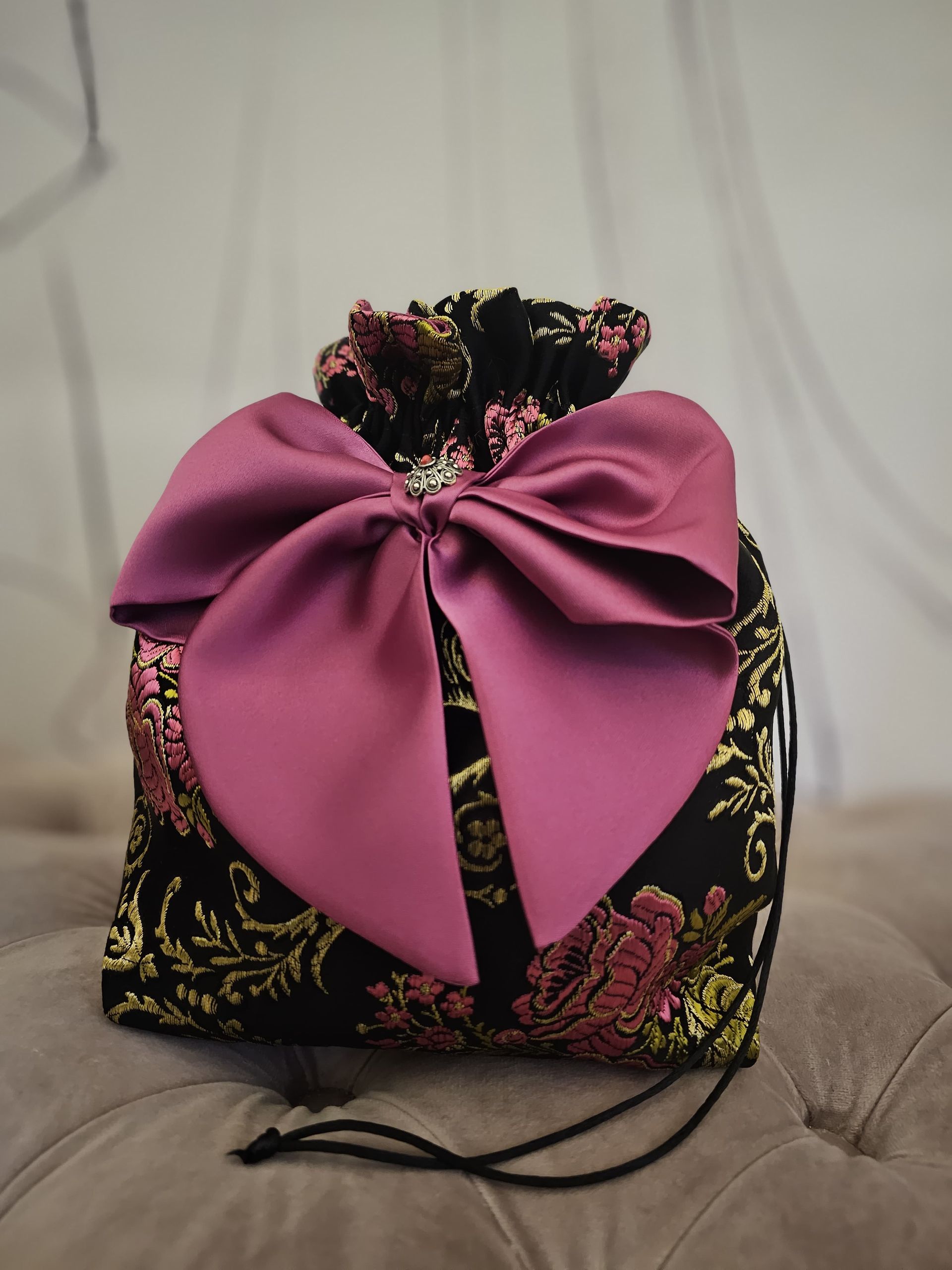 Una borsa nera con un fiocco rosa è seduta accanto a una borsa rosa