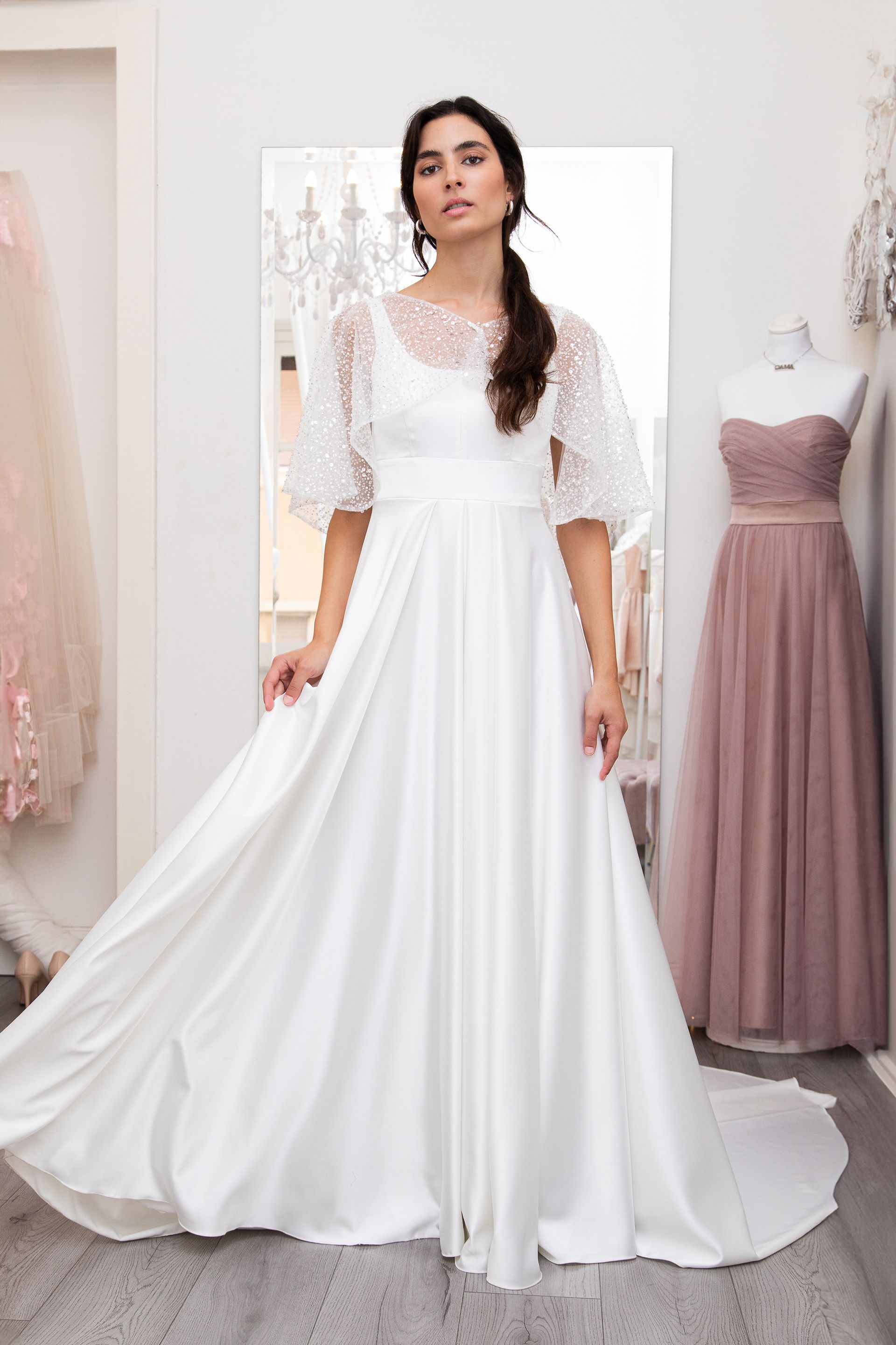 Una donna in abito da sposa bianco è in piedi davanti a uno specchio.