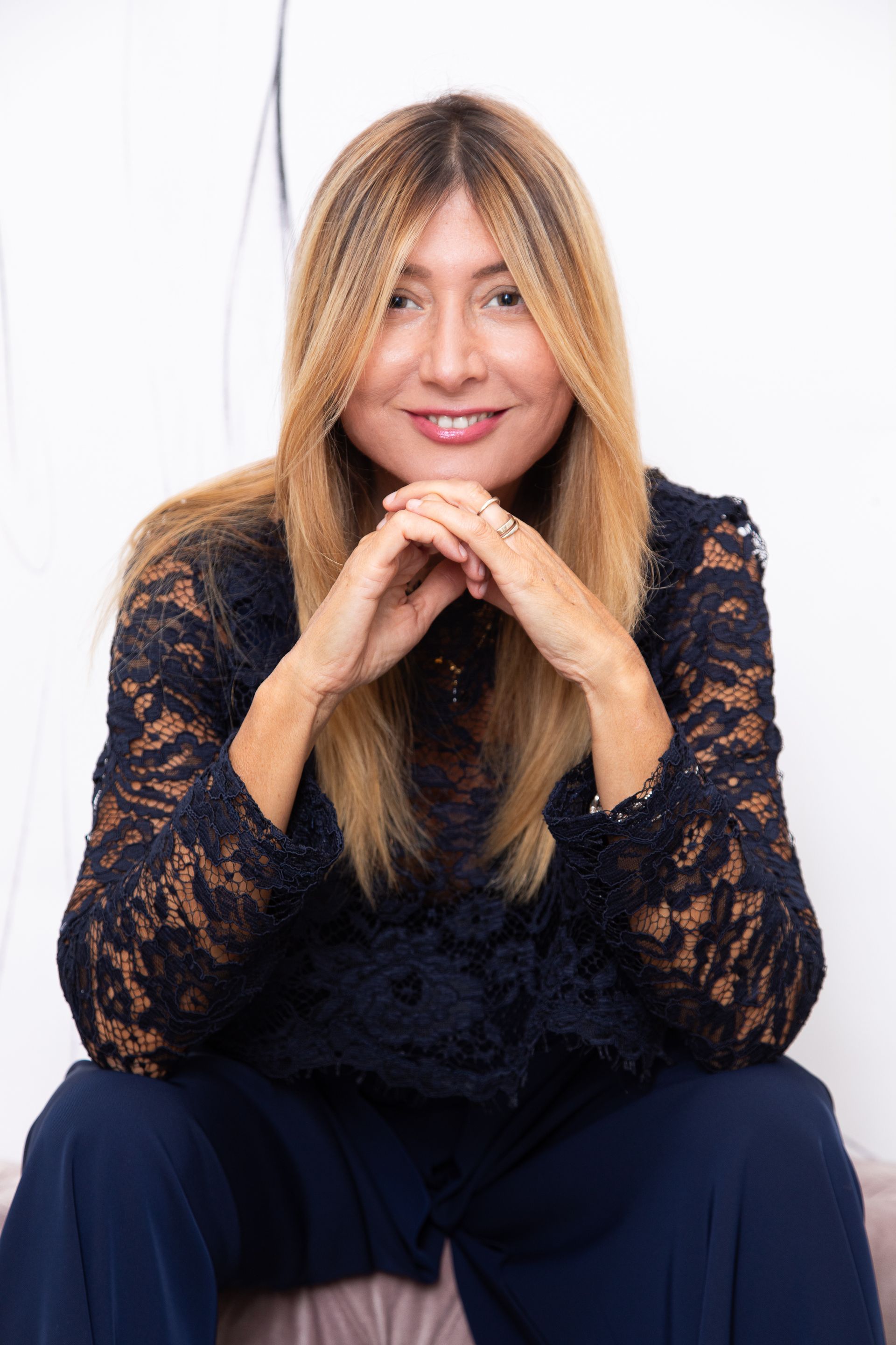 Una donna è seduta su un divano con le mani giunte e sorridente.