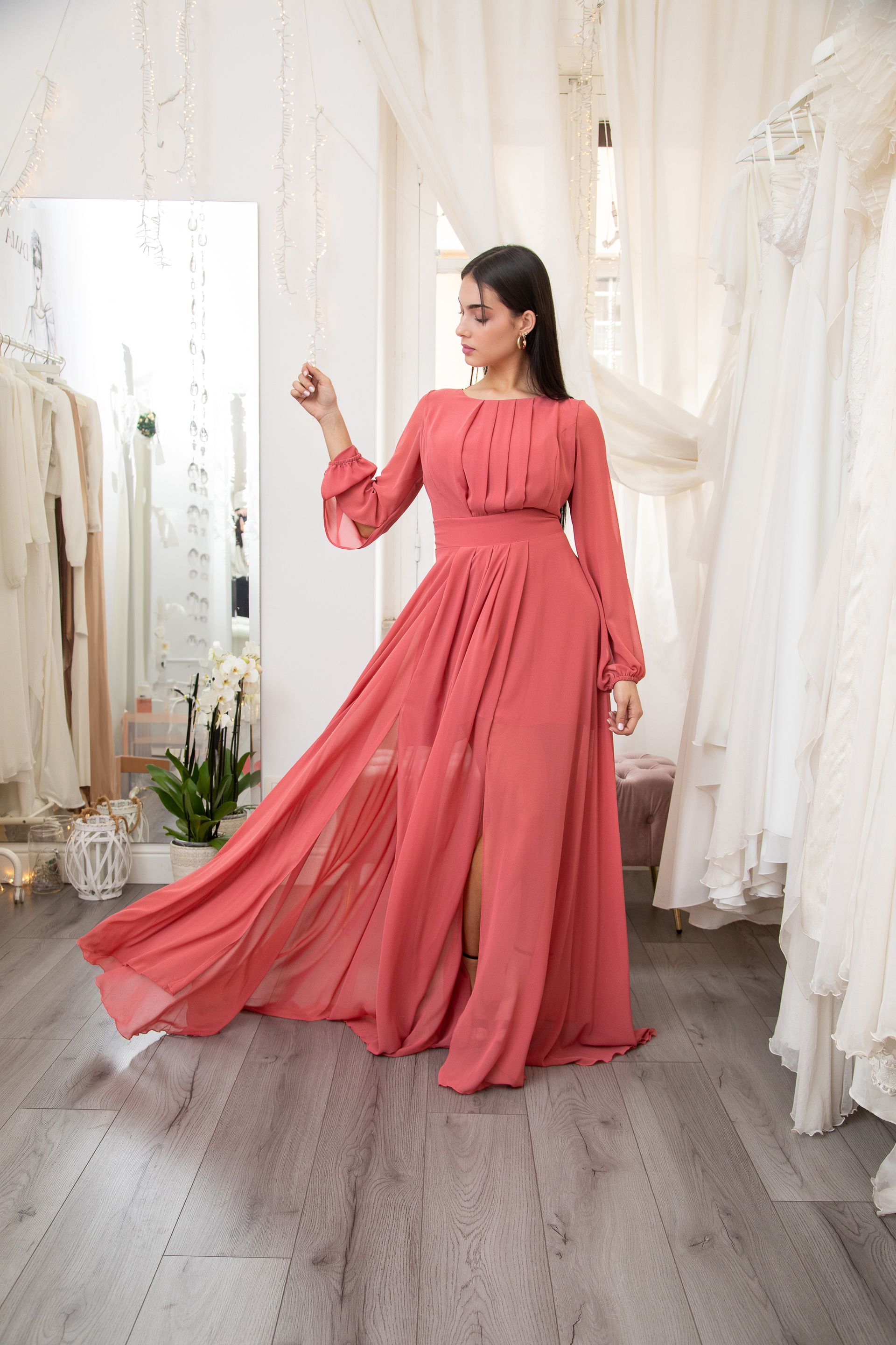 Una donna con un lungo abito rosa è in piedi davanti a uno specchio.