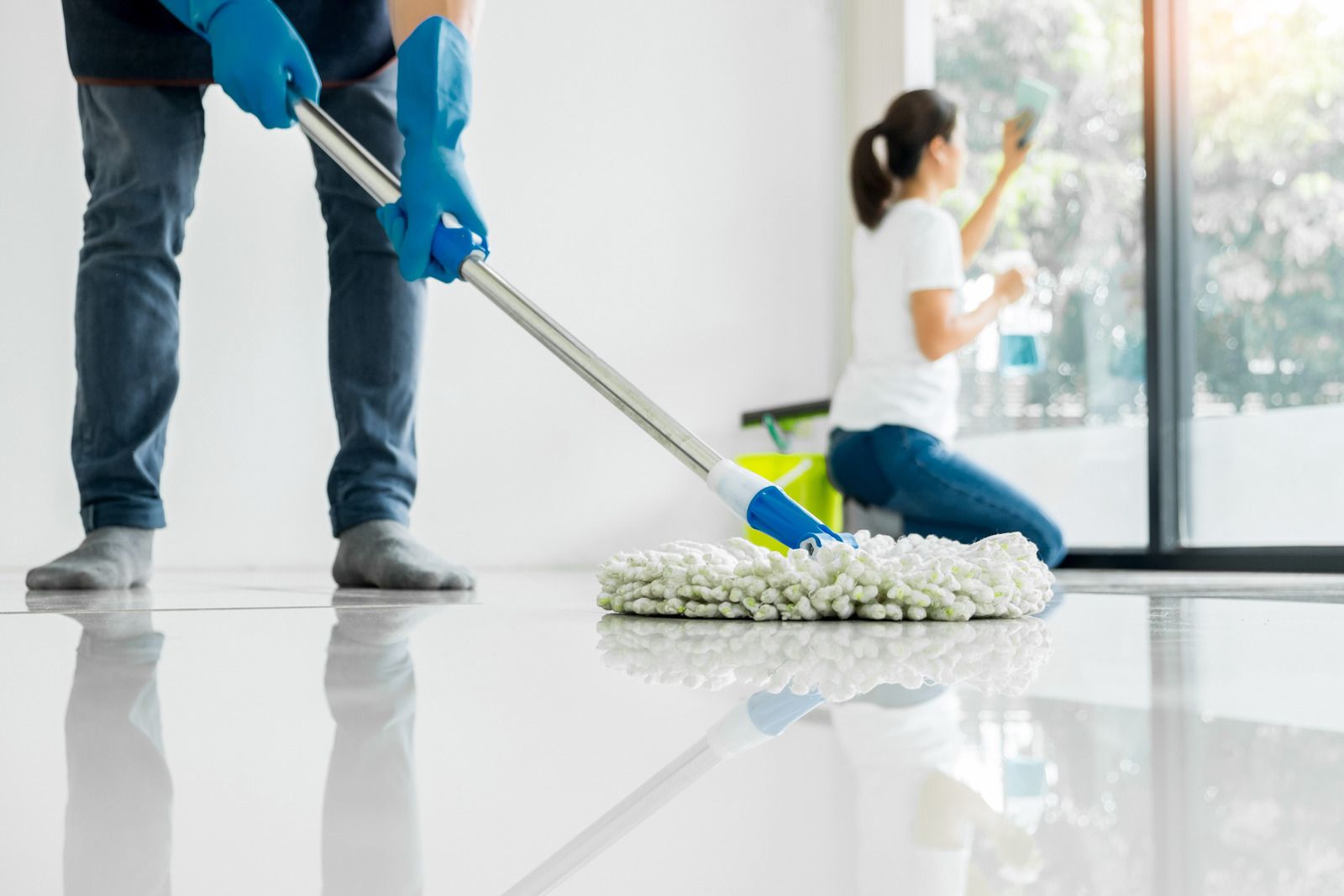 A man is mopping the floor while a woman is cleaning the windows.