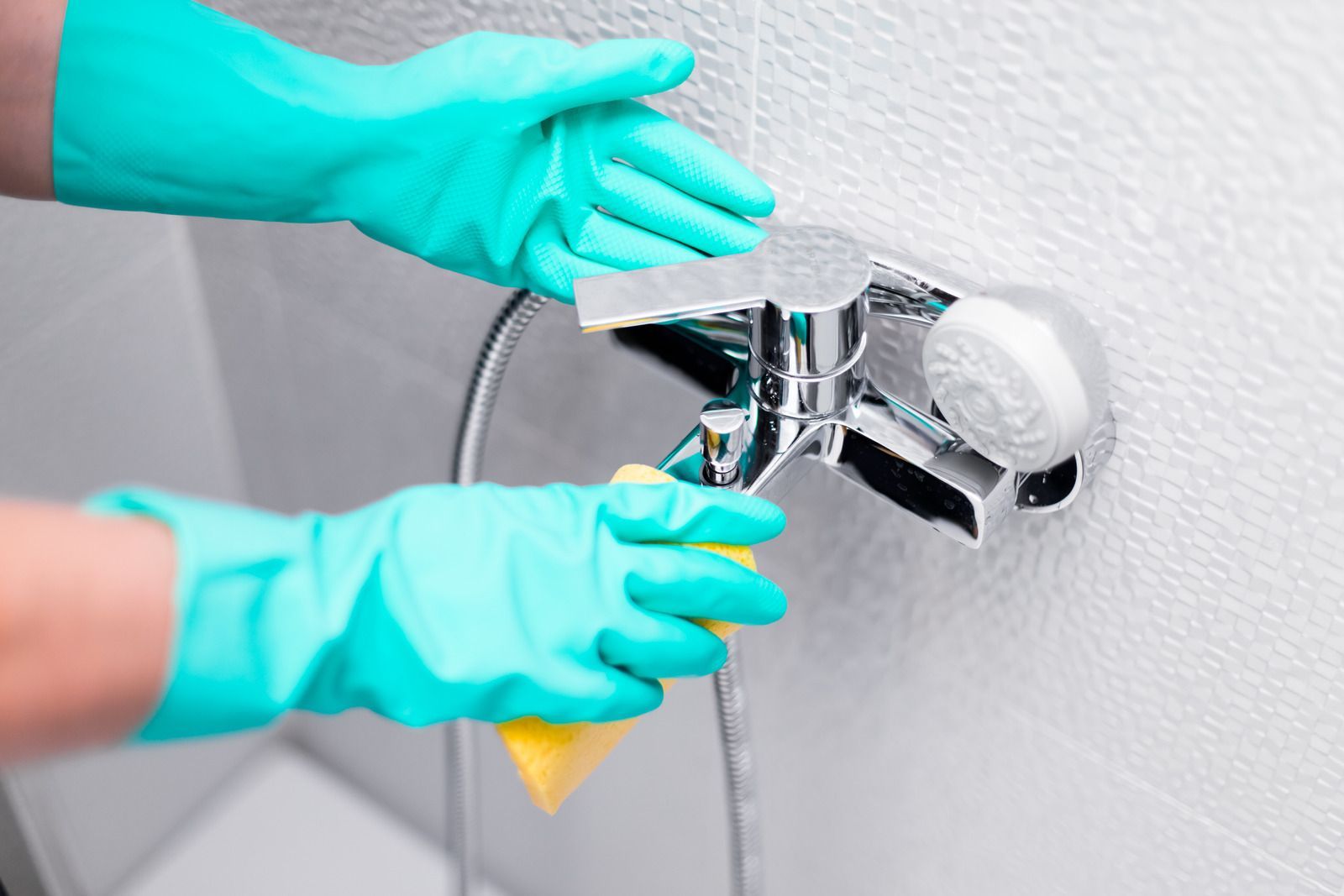 A person wearing rubber gloves is cleaning a shower faucet.