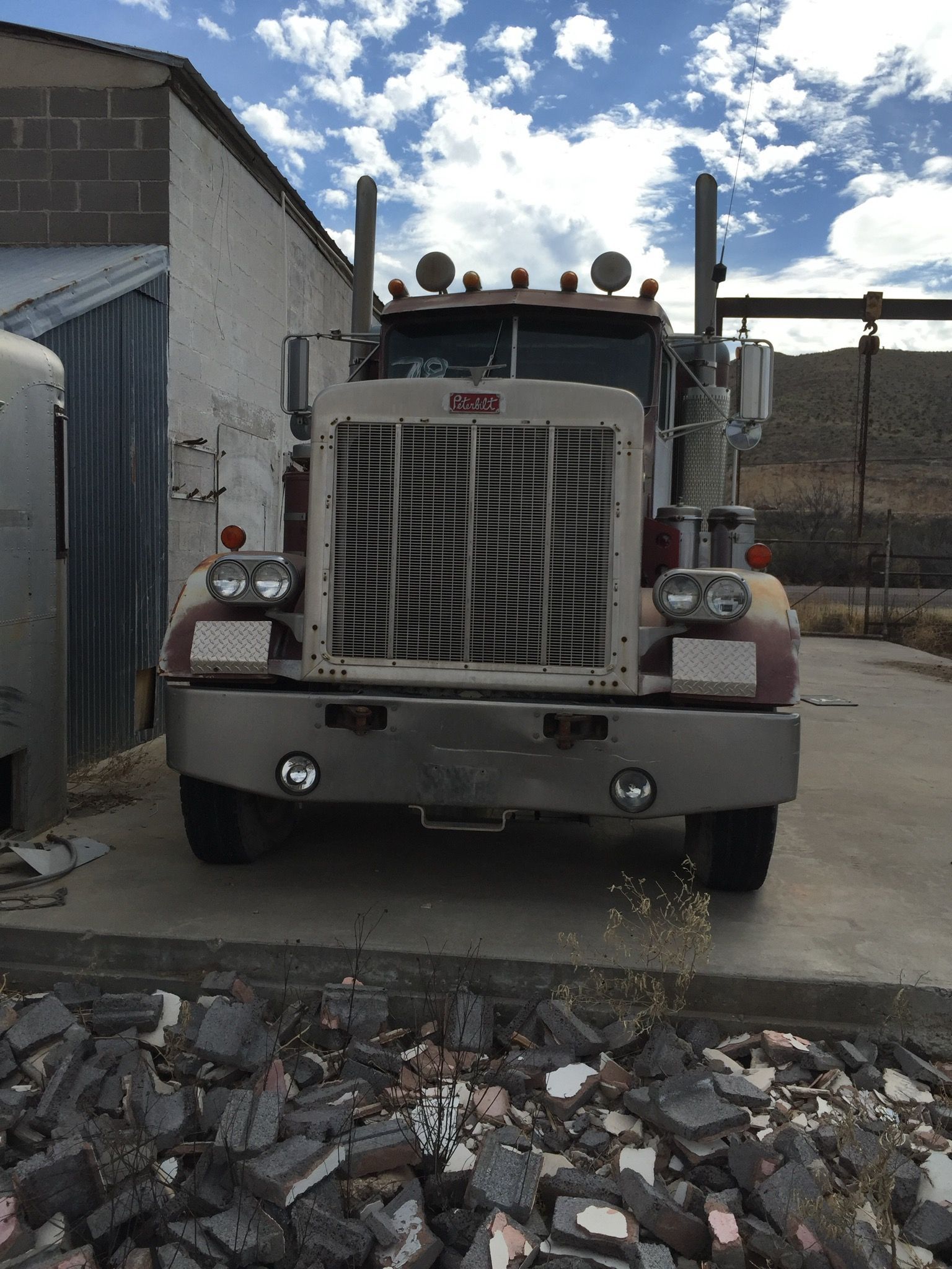 Semi-truck parked in front of a building; weathered exterior, open sky with clouds.