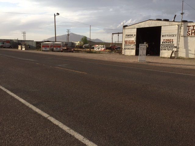 A tire shop next to a road, with a mountain in the background under a cloudy sky.