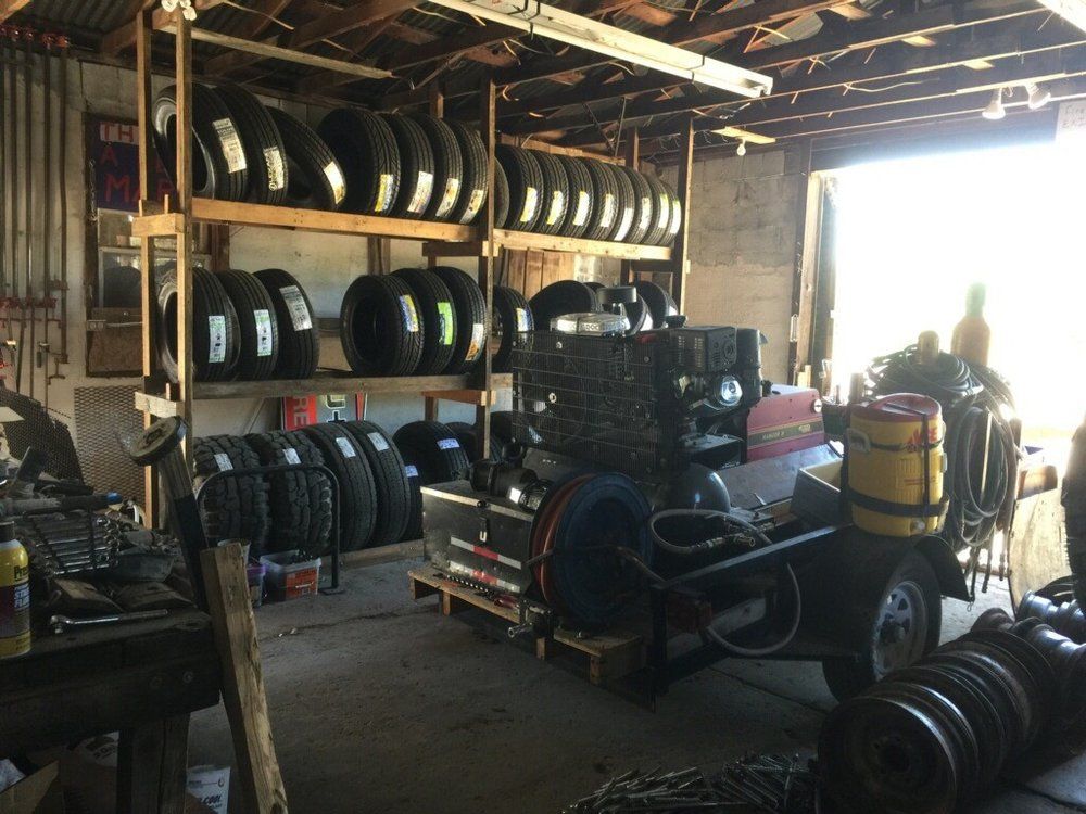 Tires stacked on wooden shelves in a cluttered garage, with tools and a trailer visible.