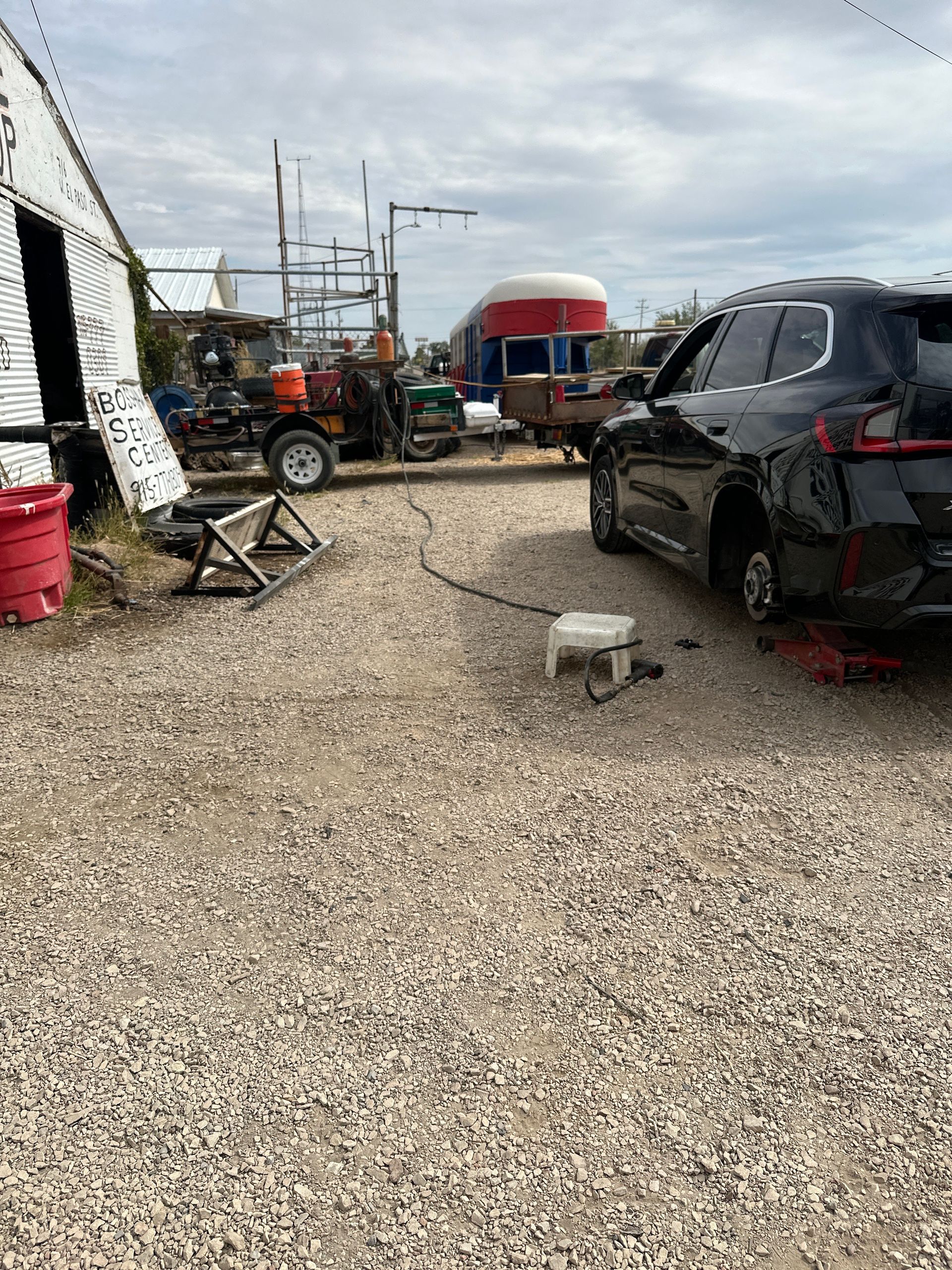 Gravel lot with a black car, tools, and a red and white structure in the background.