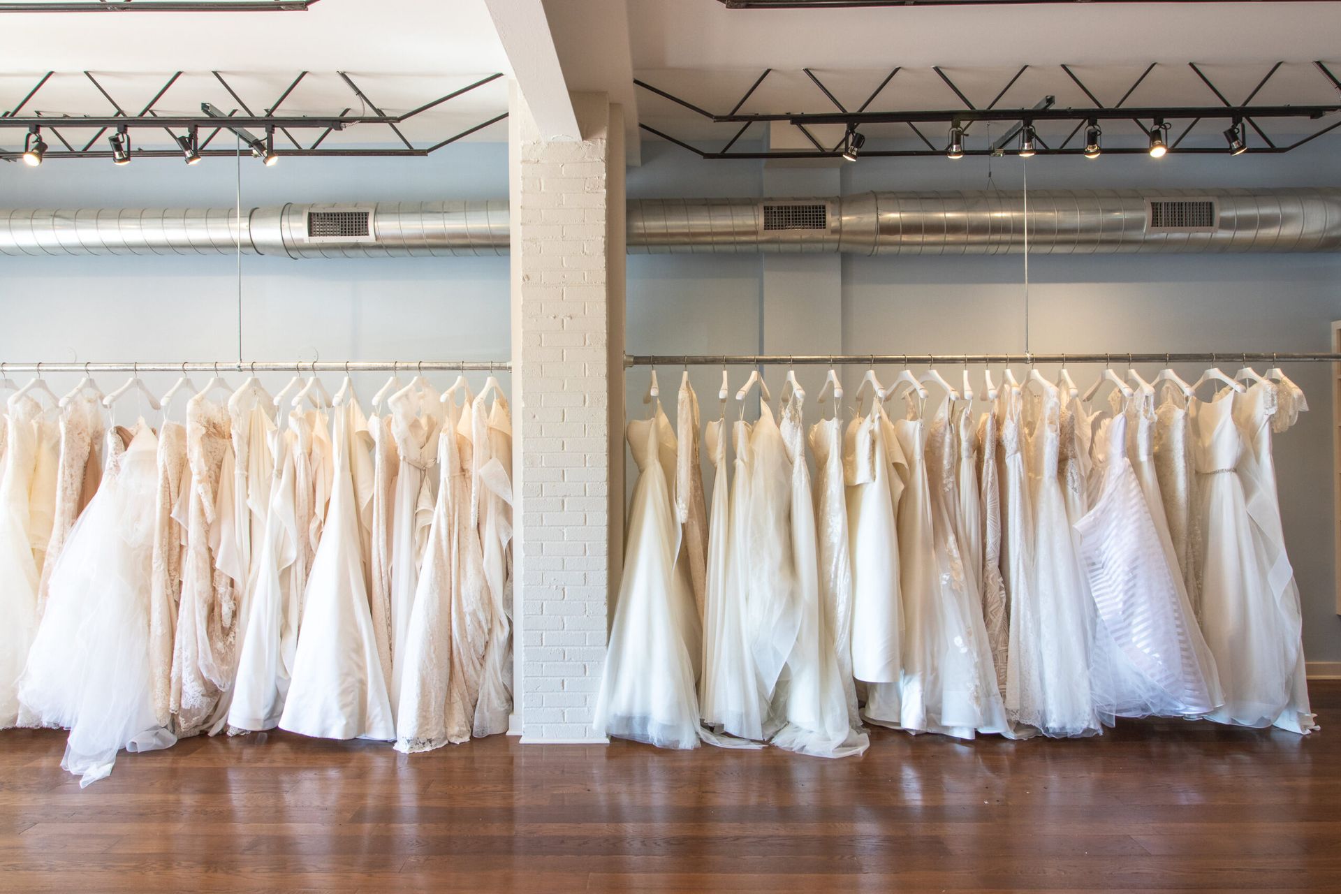 A row of white wedding dresses hanging on a rack against a light blue wall in a bright boutique.